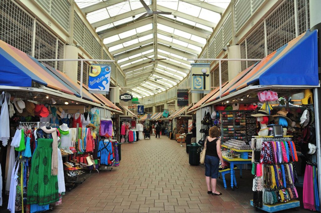 Bayside Marketplace Mall is a market style mall with lots of stalls with tourist gifts, dresses, neck scarves, colored objects hanging and a lady looking in a stall.